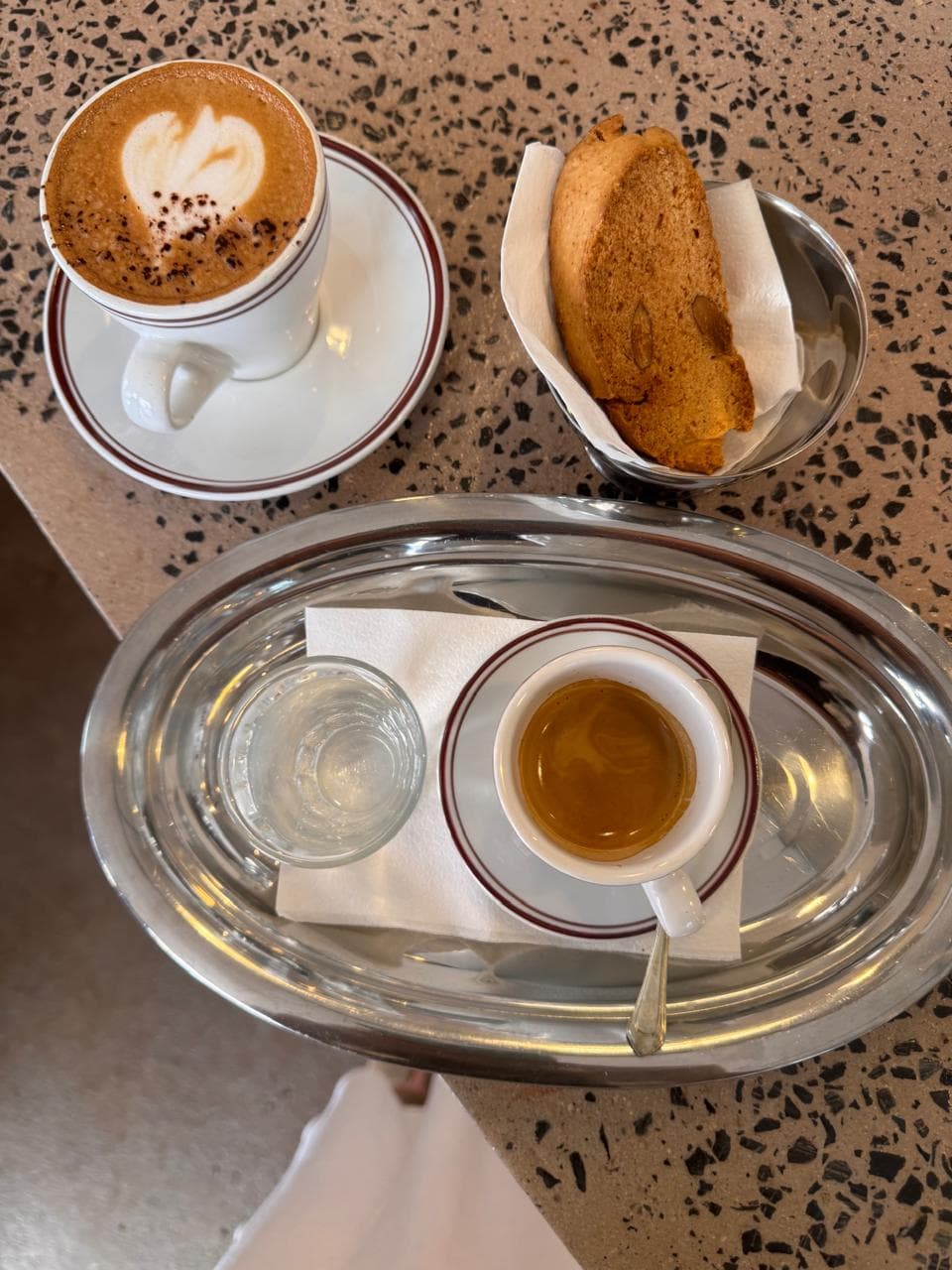 Cappuccino with biscotti and espresso served on silver tray on terrazzo counter