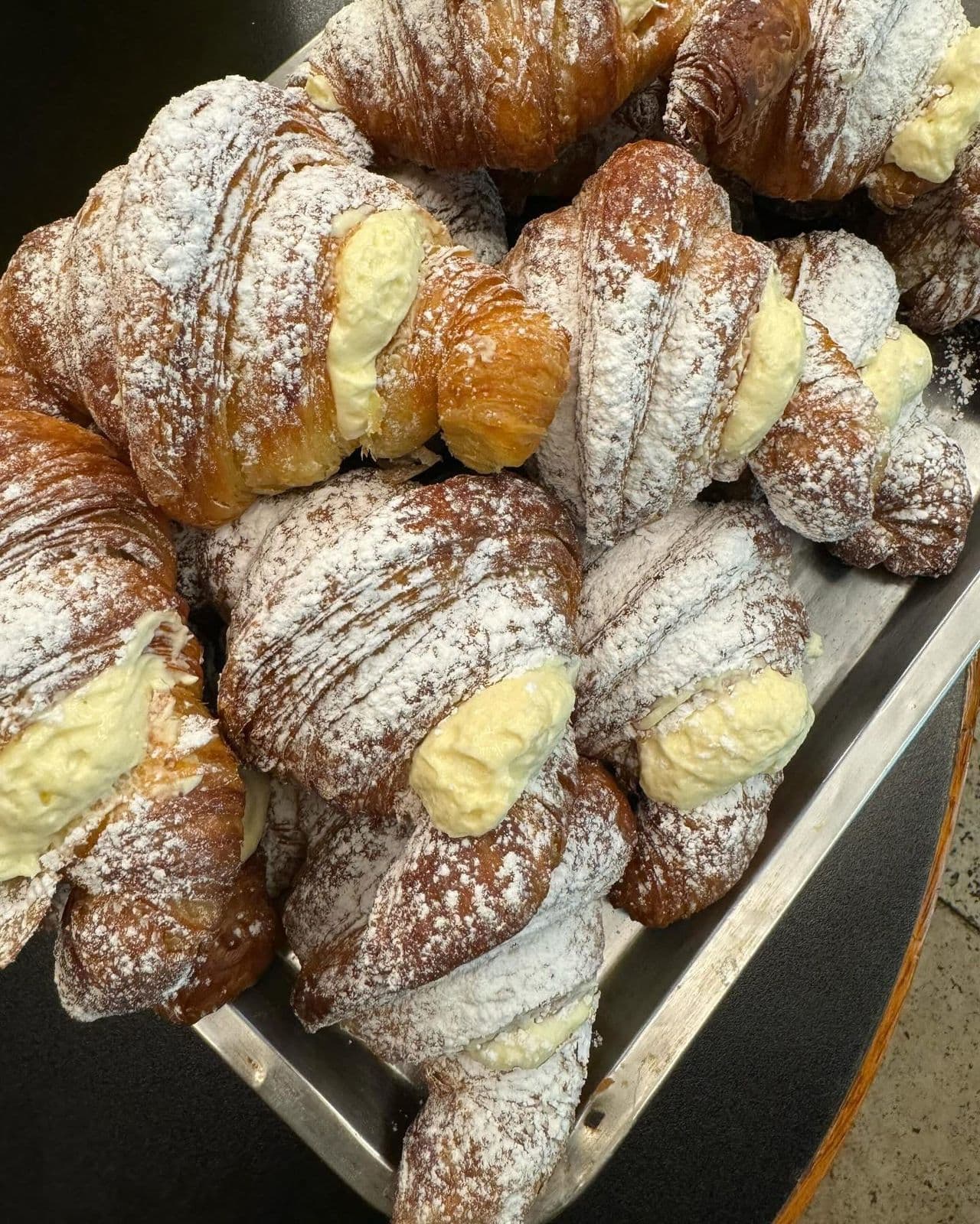 Tray of freshly baked cream-filled croissants dusted with powdered sugar