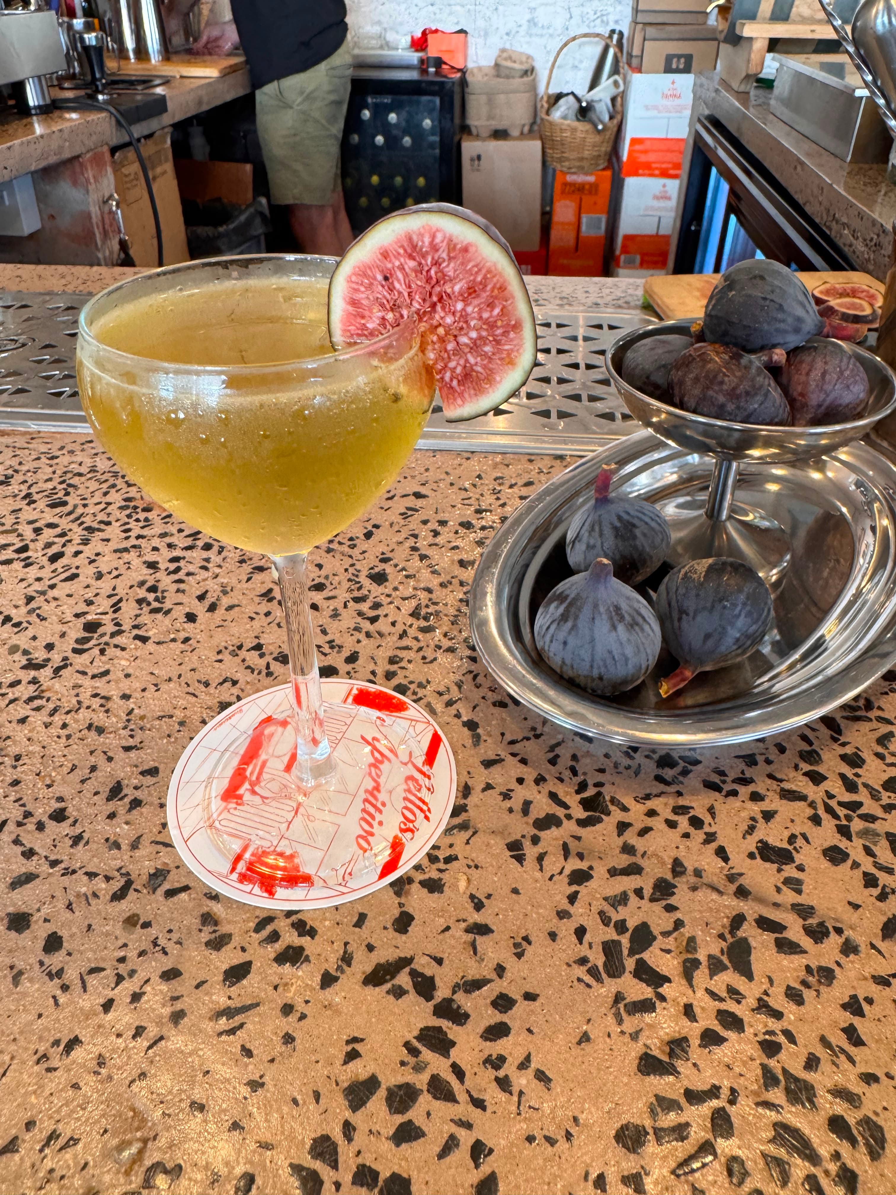 Fig cocktail on a Lello's aperitivo coaster beside a silver bowl of fresh figs at the bar
