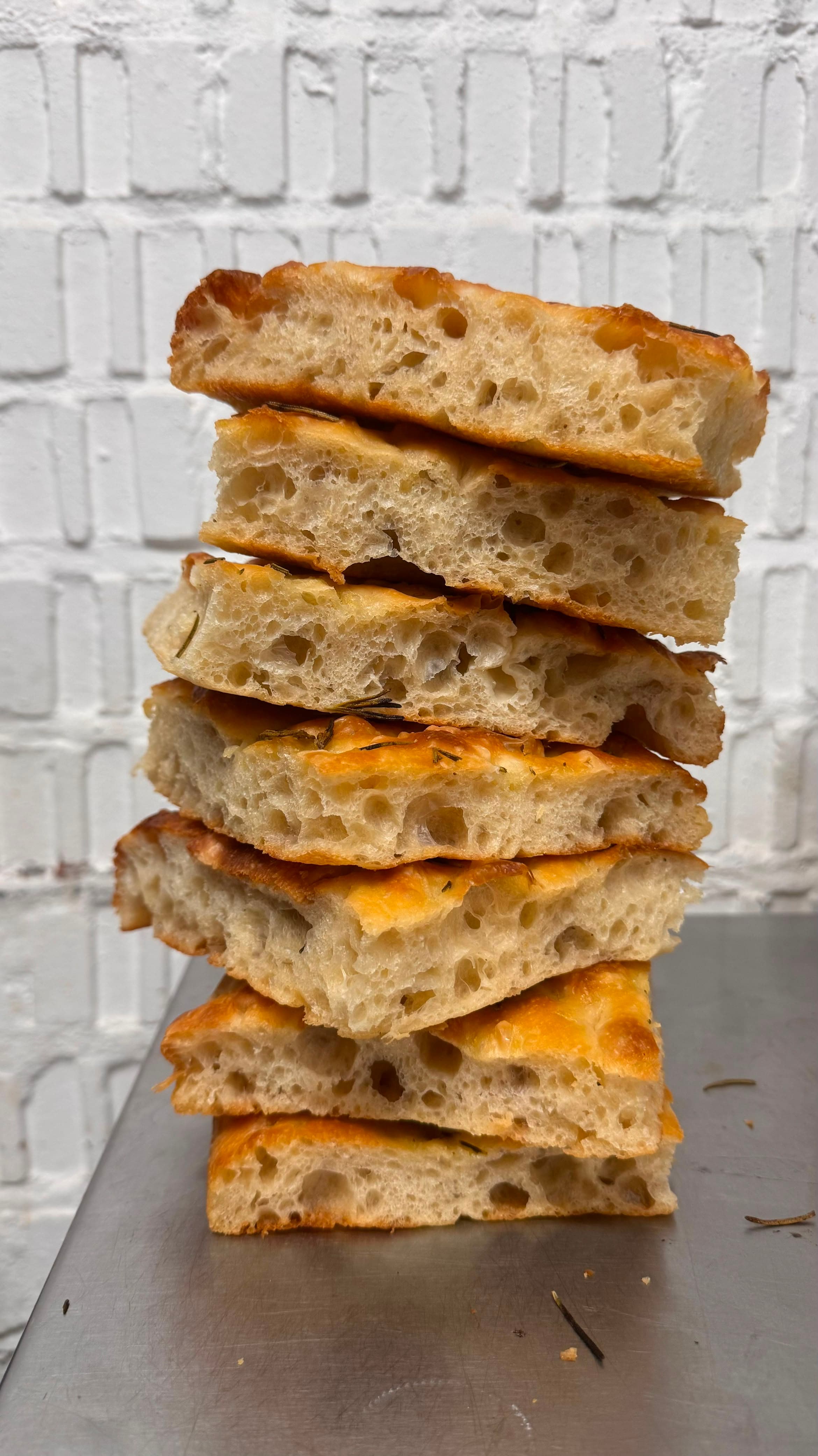 Tall stack of freshly baked rosemary focaccia slices on a steel counter