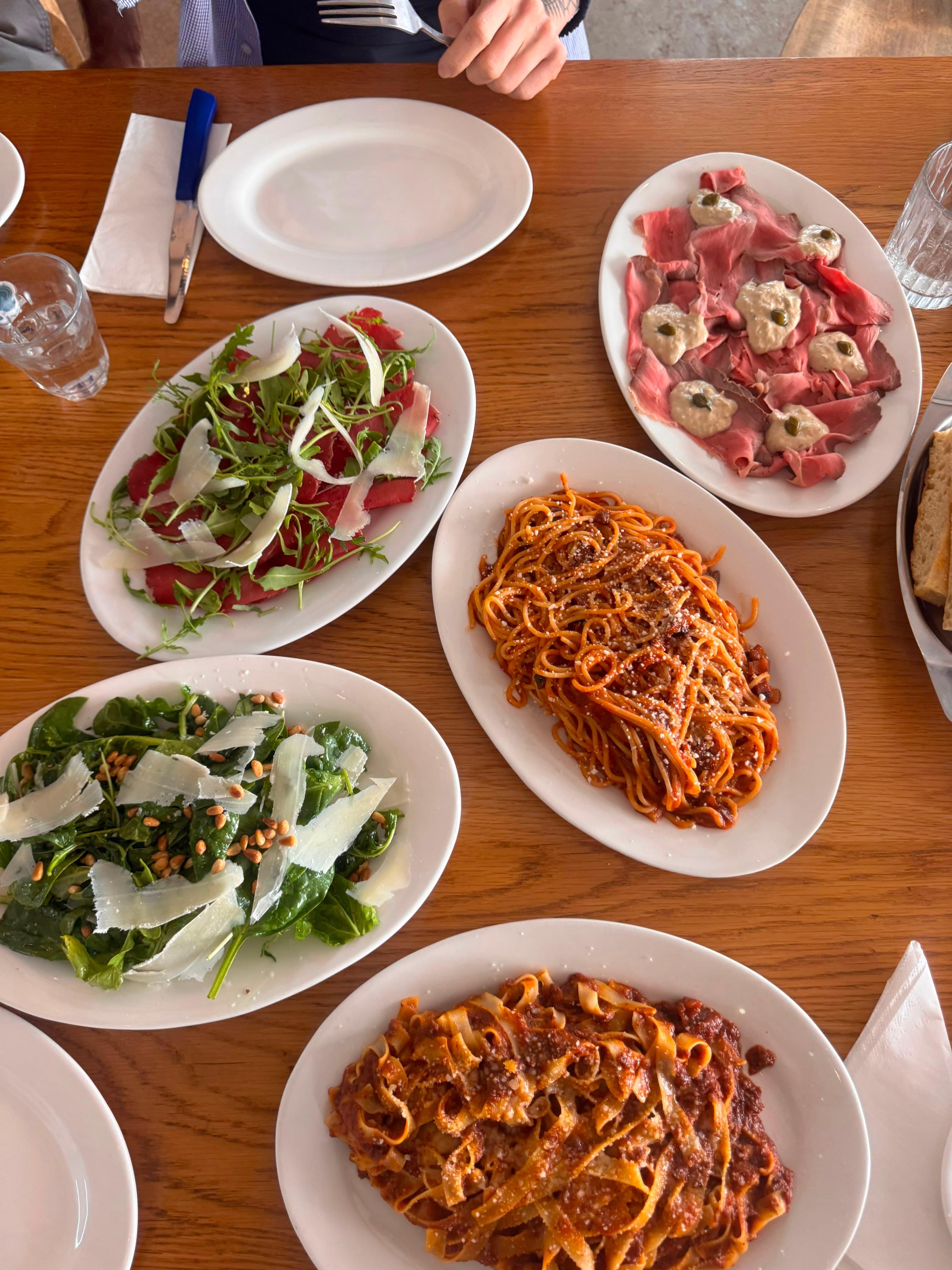 Table spread of pasta al ragu, salads and carpaccio shared family style