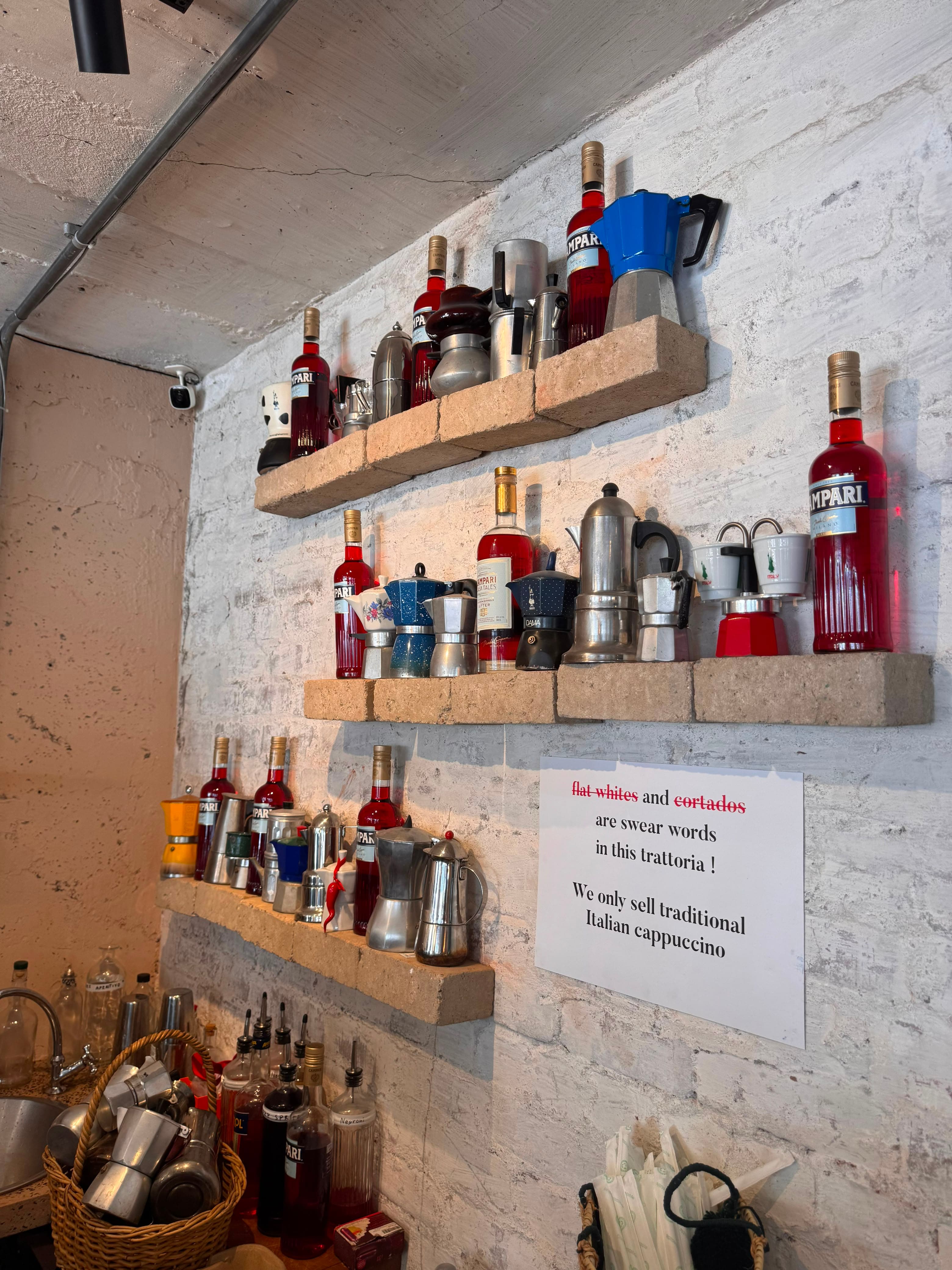 Brick shelves lined with moka pots and Campari bottles behind the bar