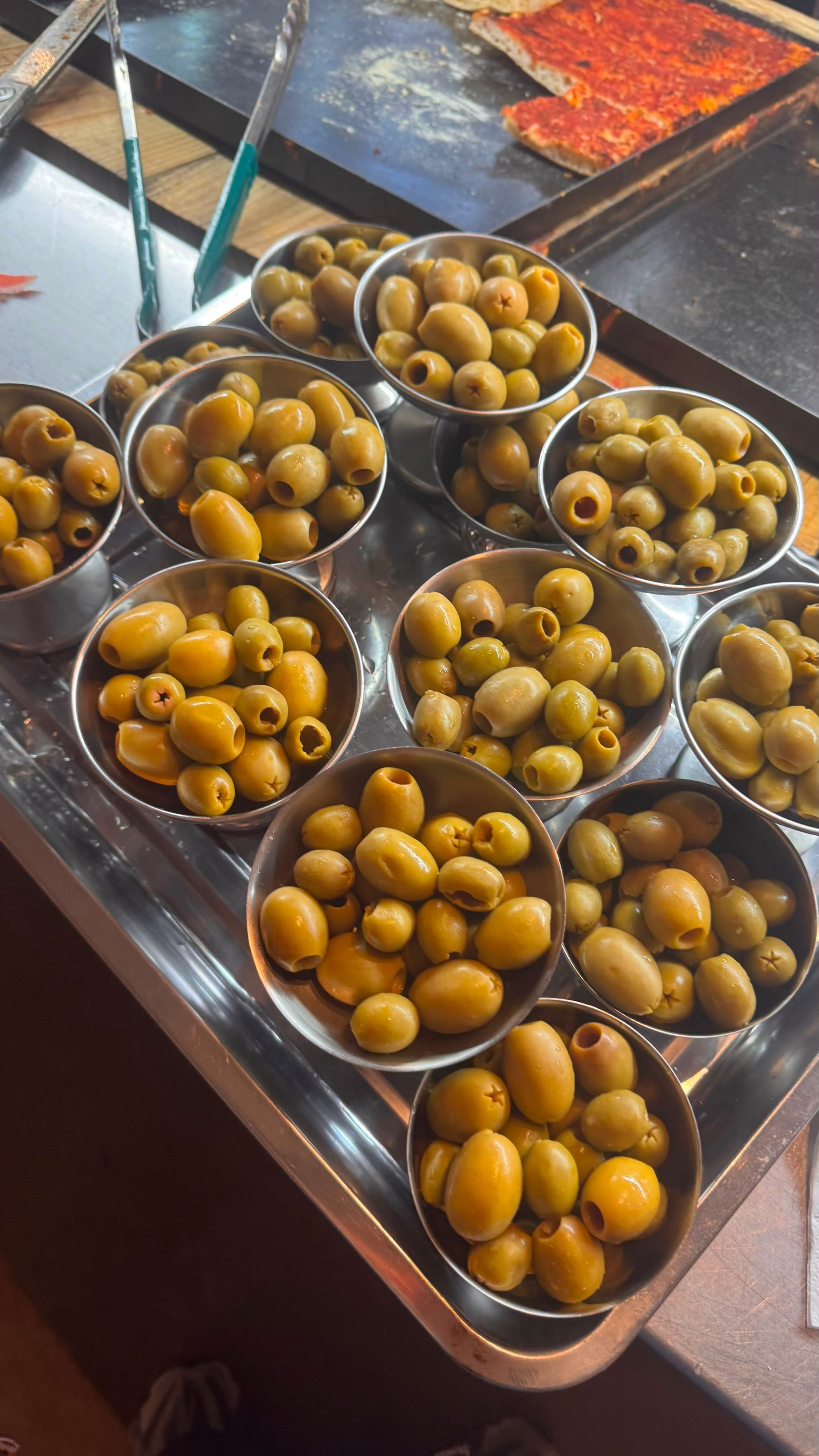 Silver bowls filled with marinated green olives lined up on a tray at the counter