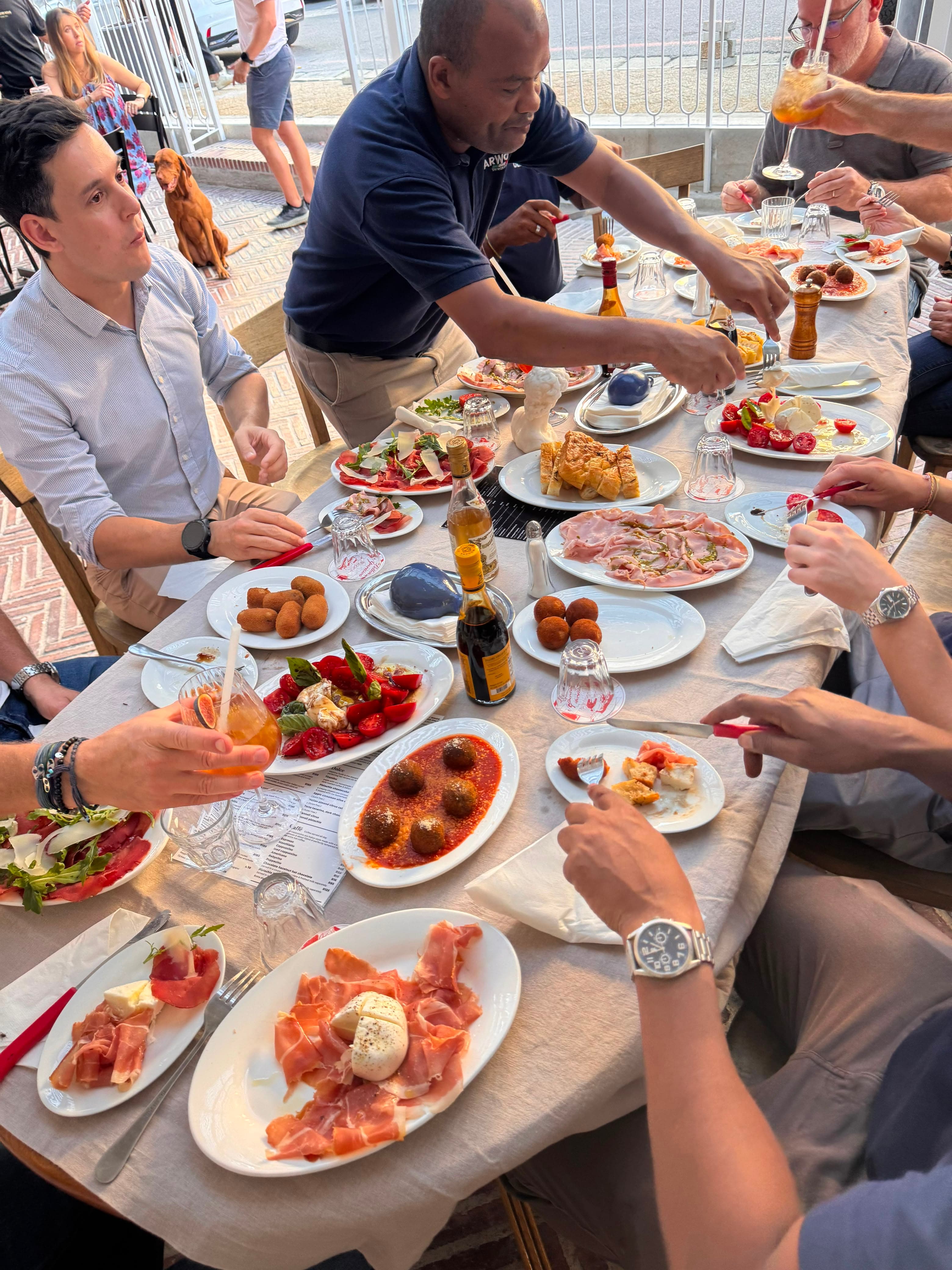 Friends sharing an outdoor table covered with antipasti, suppli and burrata plates