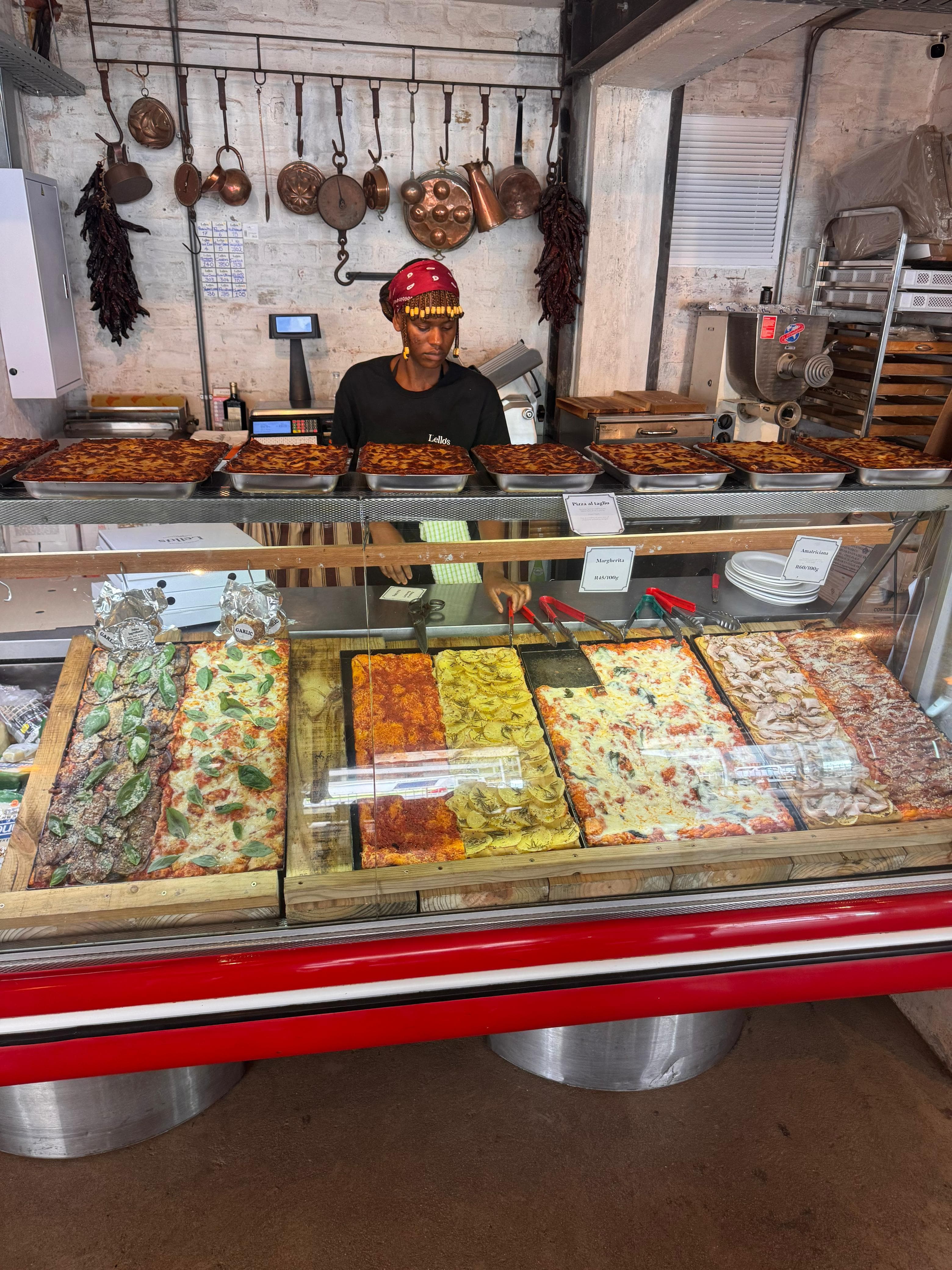 Lello's Trattoria pizza al taglio counter with copper pans and staff serving