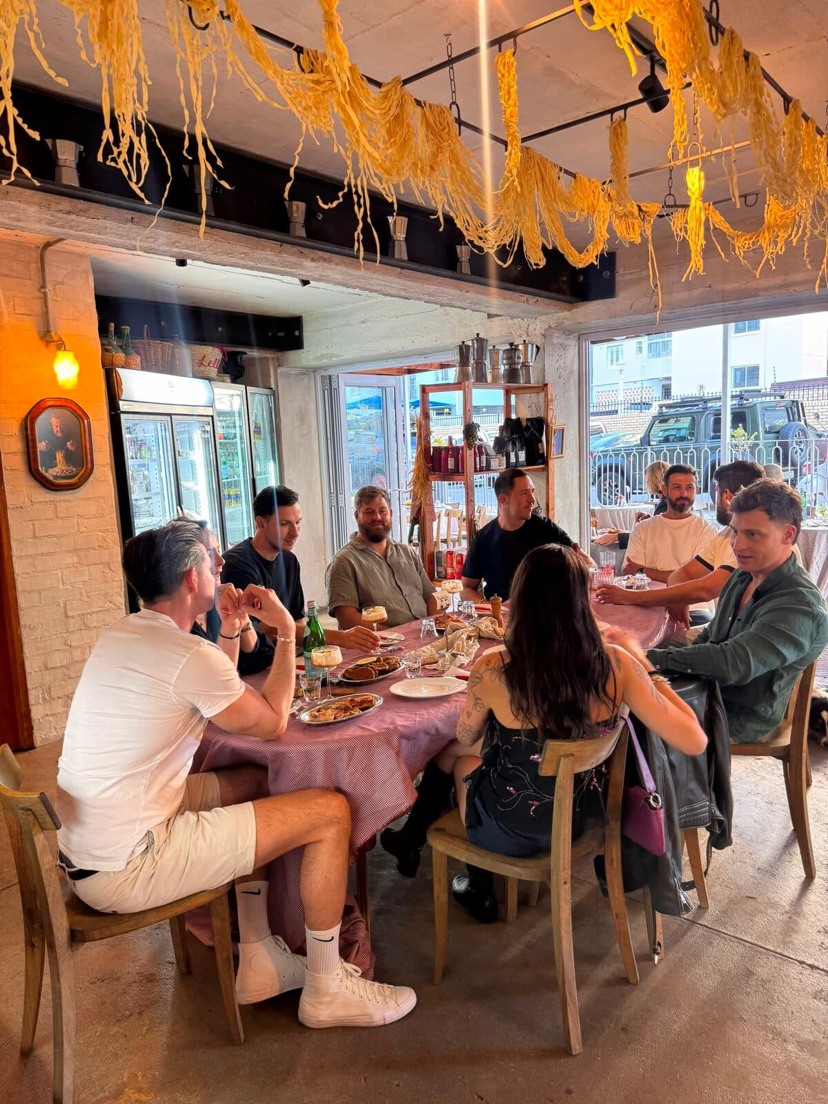 Guests sharing a family-style dinner at Lello's beneath hanging fresh pasta