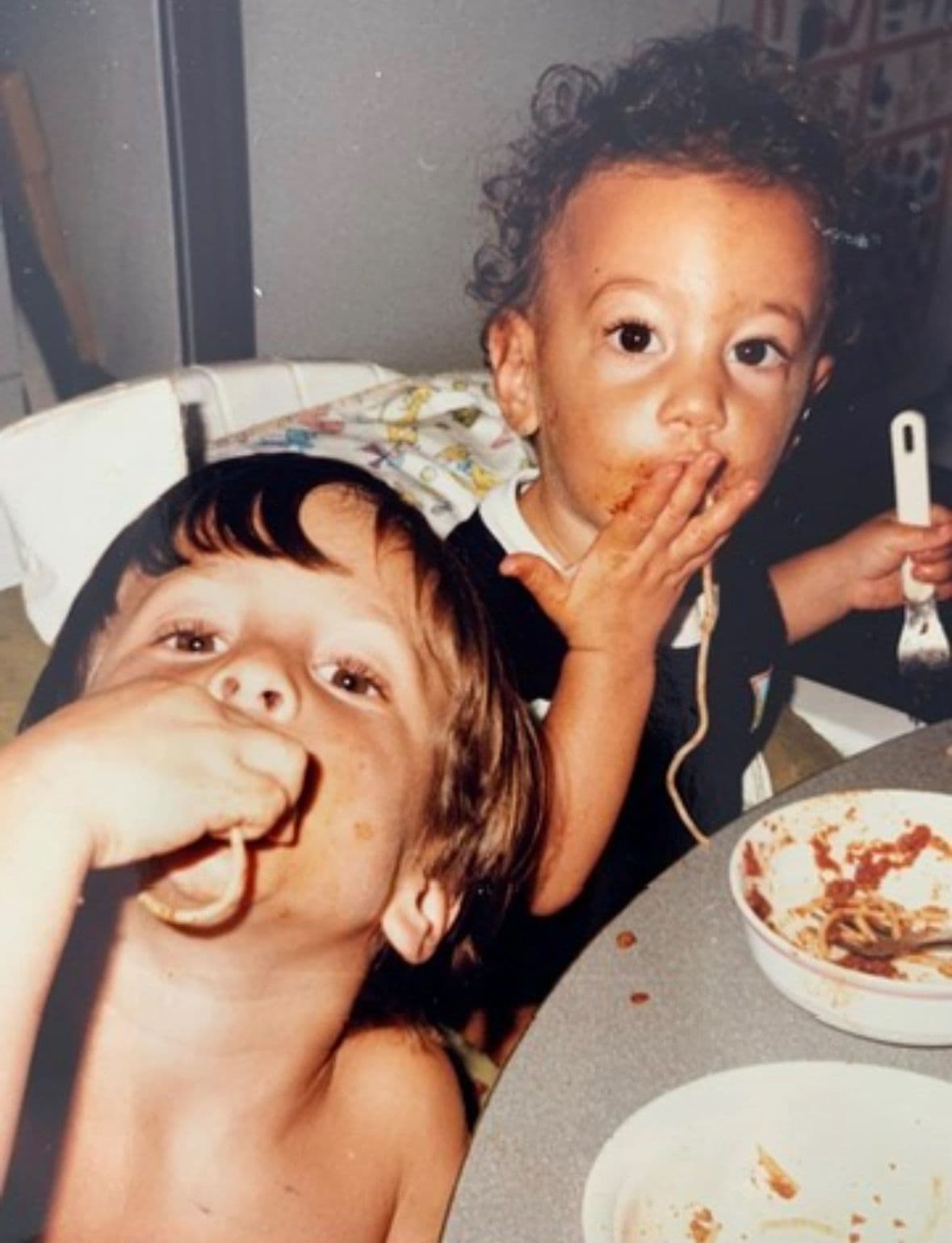 Two children joyfully eating spaghetti with messy faces