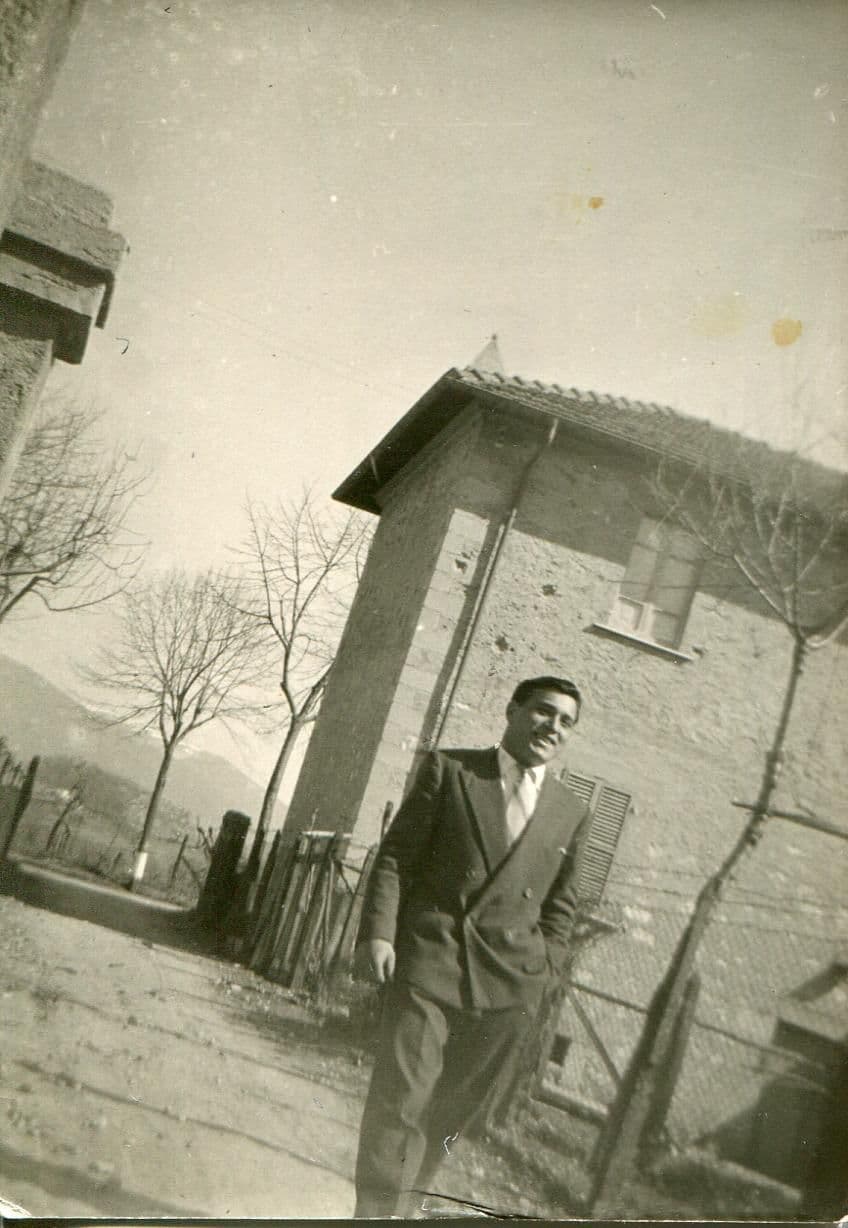 Black and white portrait of a young man in a suit outside an Italian house